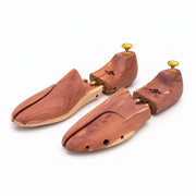 Pair of adjustable aromatic cedar wood shoe trees with gold brass heel knobs on white background